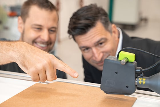 Adhesive application (hot melt stitching) with Volta application head in the foreground – satisfied faces of machine operator and businessman in the background